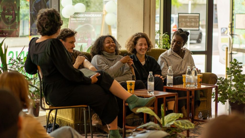 4 people on a couch at a panel talk laughing while a moderator speaks from a chair
